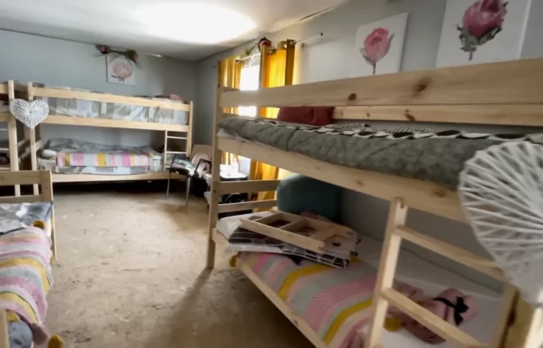 A neatly arranged room with three wooden bunk beds, colorful bedding, and several decor items including flower-themed wall art and heart-shaped ornaments. Yellow curtains cover the window.