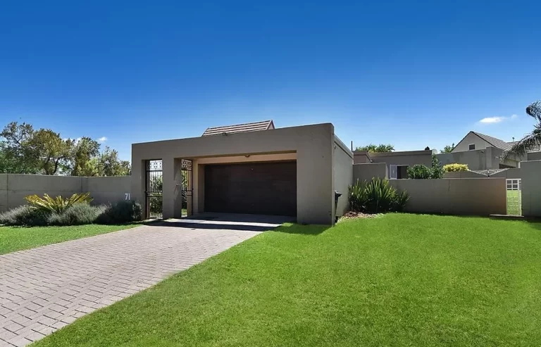 A modern single-story house with a flat roof, an attached two-car garage, and a well-maintained front lawn on a sunny day.